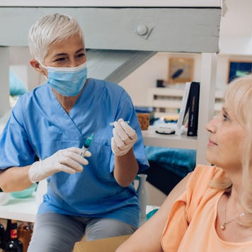 An older nurse drawing blood from a woman.