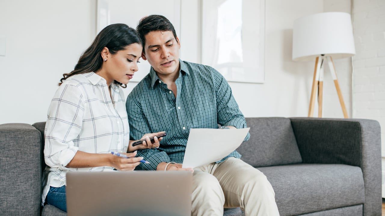 A man and woman sitting together on the couch reviewing their financial documents.