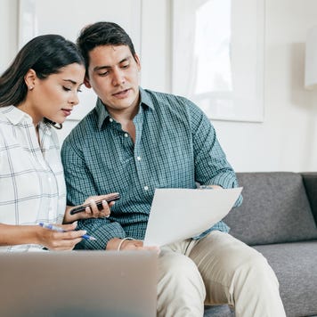 A man and woman sitting together on the couch reviewing their financial documents.