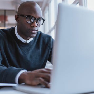 Man with glasses sitting at desk using laptop