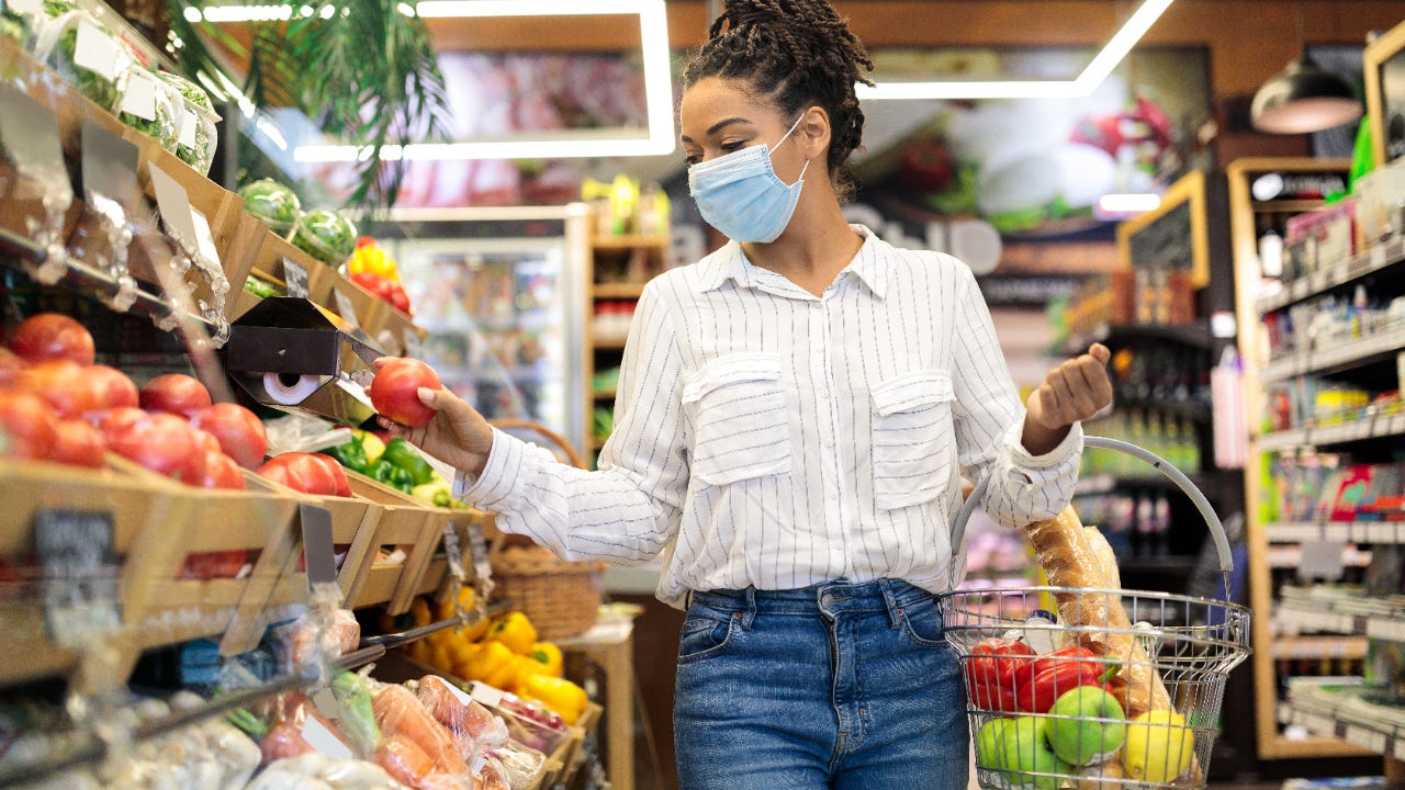 Woman choosing fresh vegetables in supermarket, walking with basket full of food along shelves in store aisle
