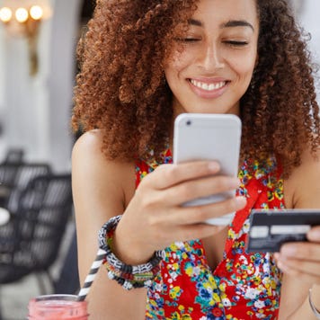 Smiling young woman holding phone and credit card