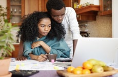 A young Black couple looks over a laptop computer and some papers