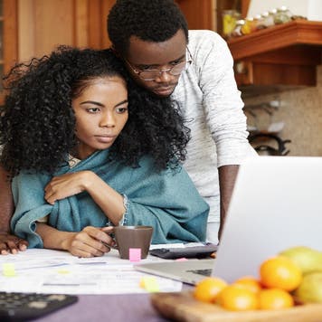 A young Black couple looks over a laptop computer and some papers
