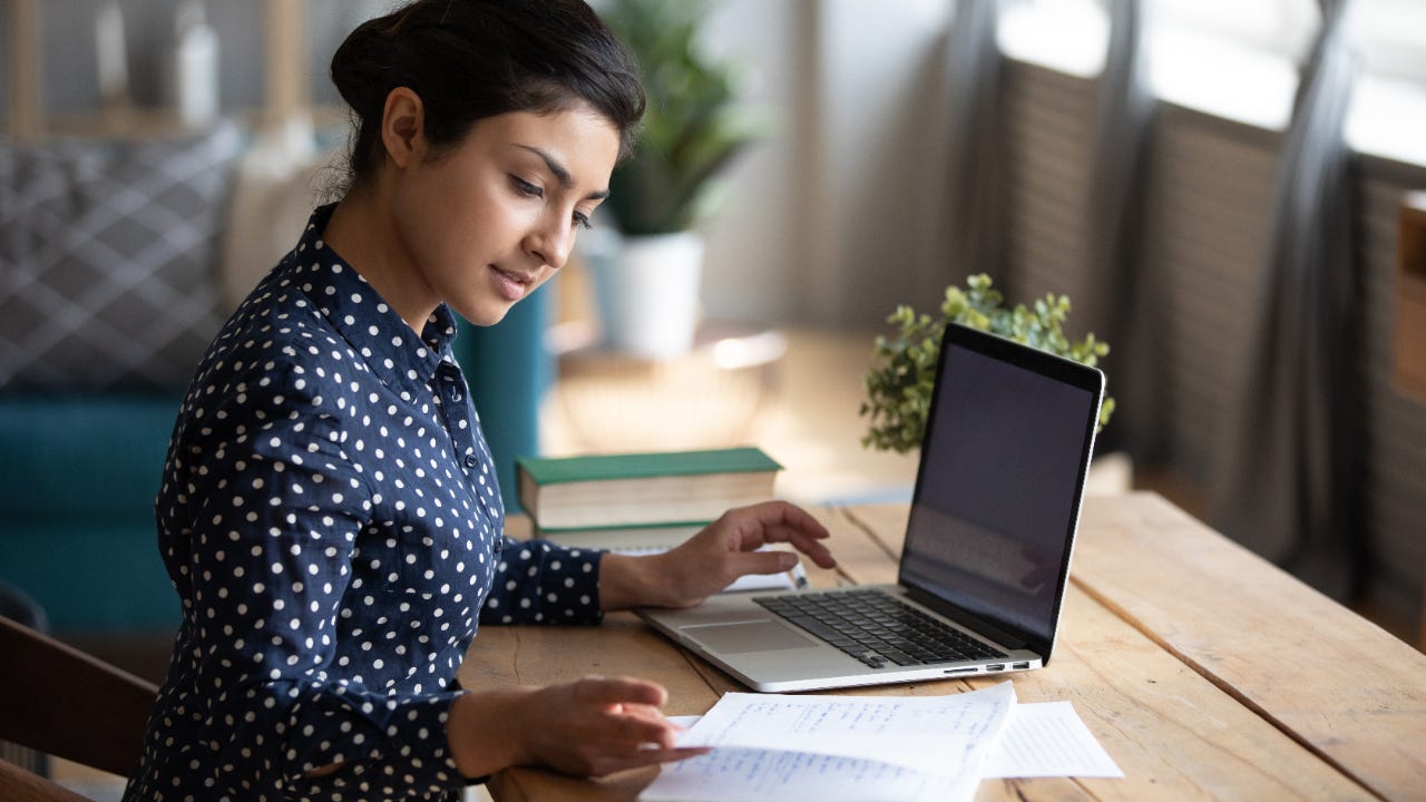 Girl sitting at desk in living room study on laptop making notes