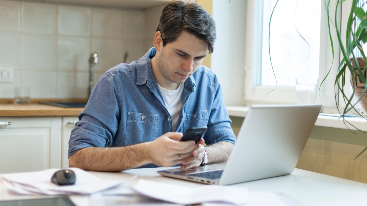 Man with paperwork and phone in front of laptop
