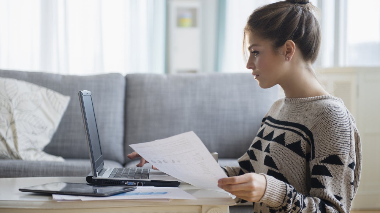 A young woman sits in front of a laptop looking at her insurance papers.