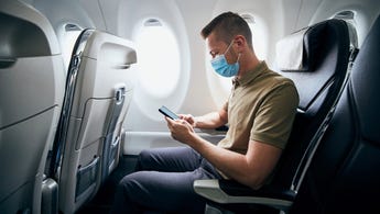Man wearing face mask and using phone on airplane