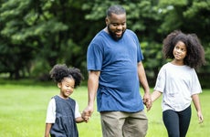 A black dad walking in a park with his two young daughters