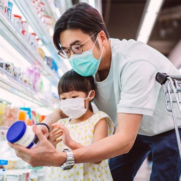 man and young child in a grocery store aisle looking at a jar of food
