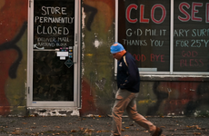 A person passes a closed storefront in Patchogue, New York