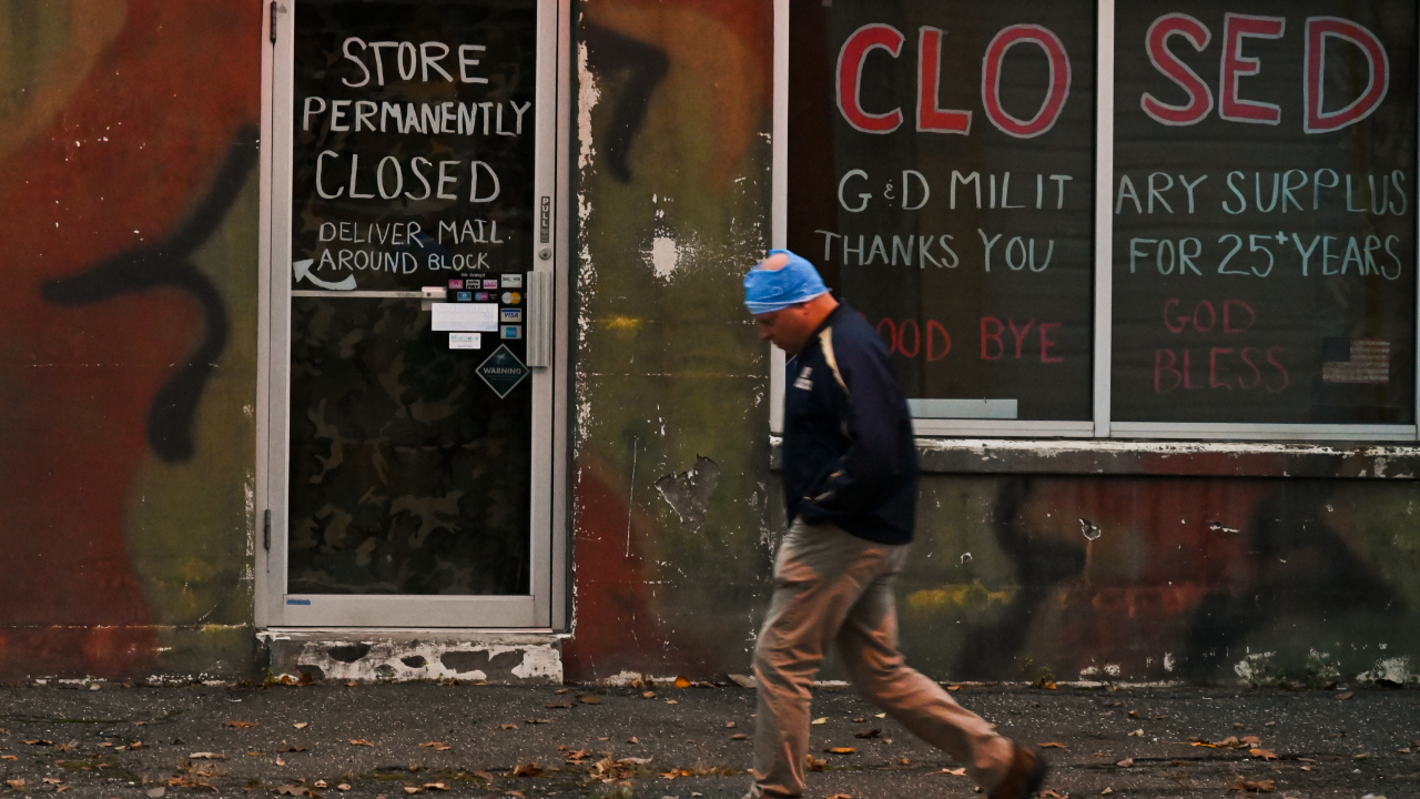 A person passes a closed storefront in Patchogue, New York
