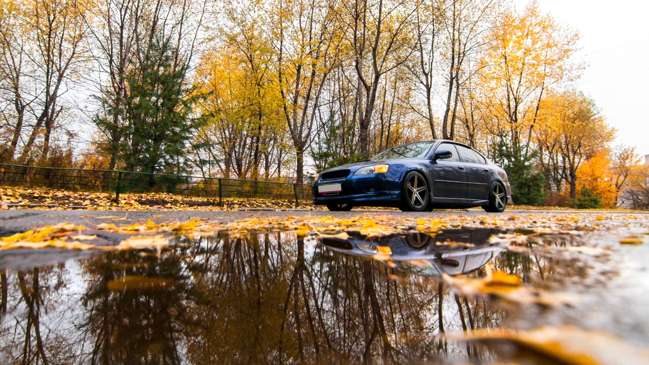 Blue Subaru on autumn road in rainy day