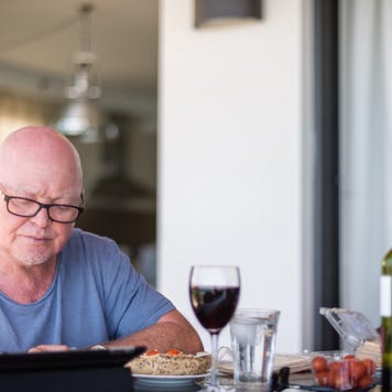 An older man researches online while having a glass of wine.