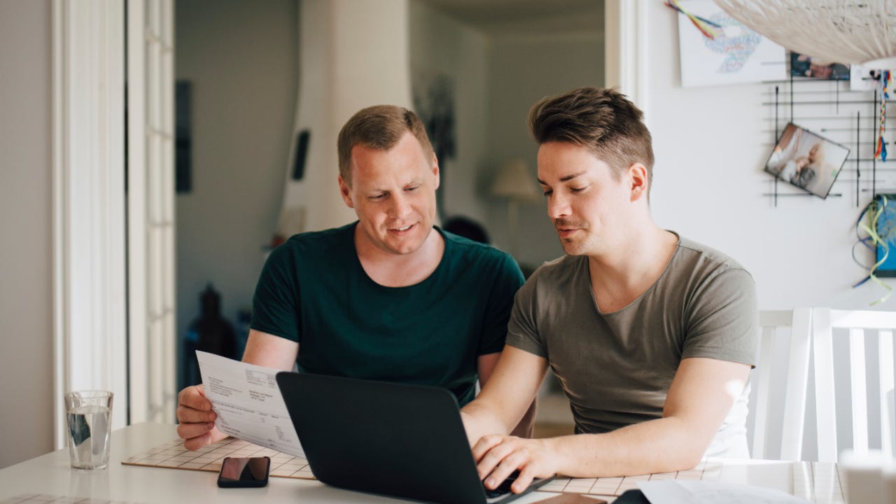 Smiling male gay couple paying bill through laptop on dining table at home
