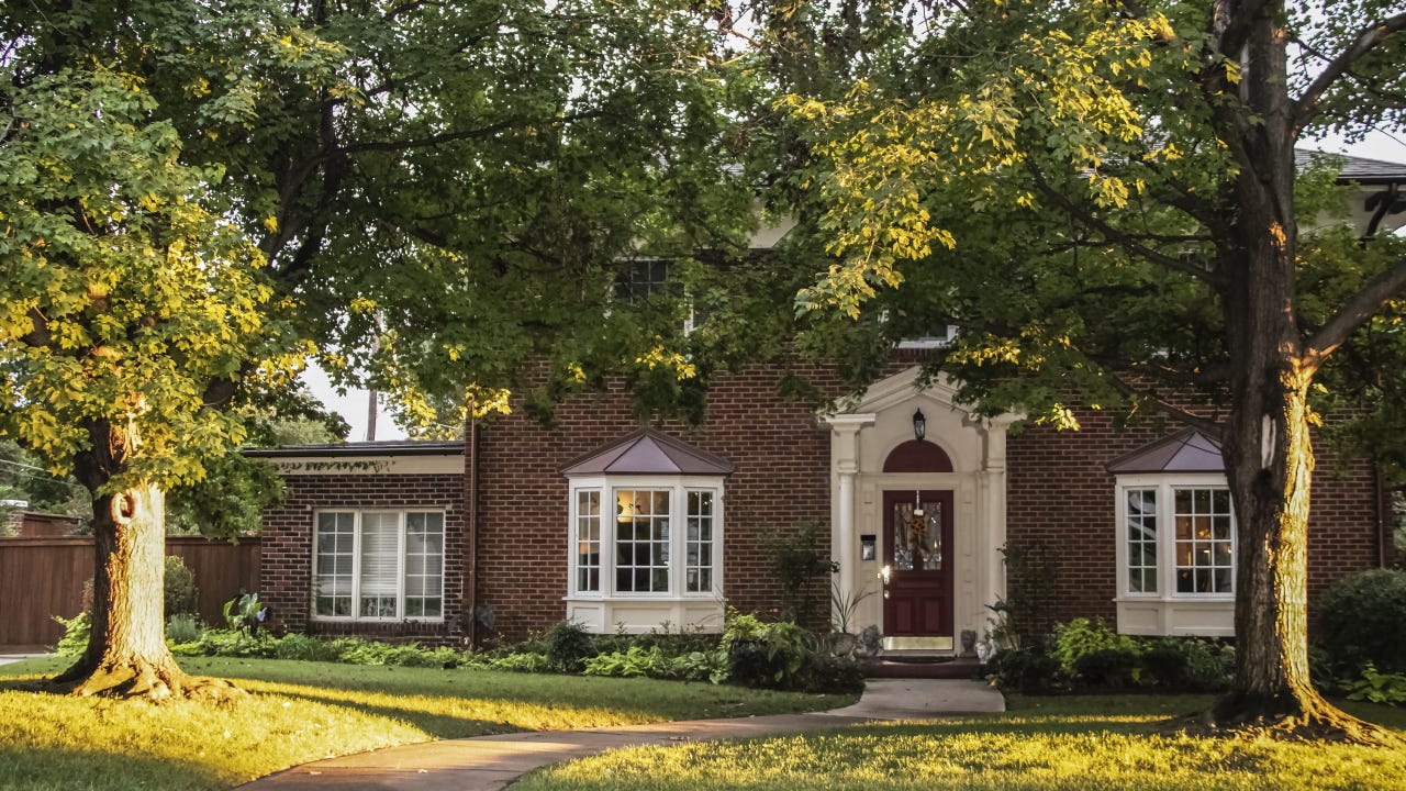 Golden Hour on the maple trees in front of traditional brick house with columns and bay windows - light stretching across front yard and up tree trunks