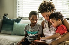 A Black mother using tablet with young sons on couch