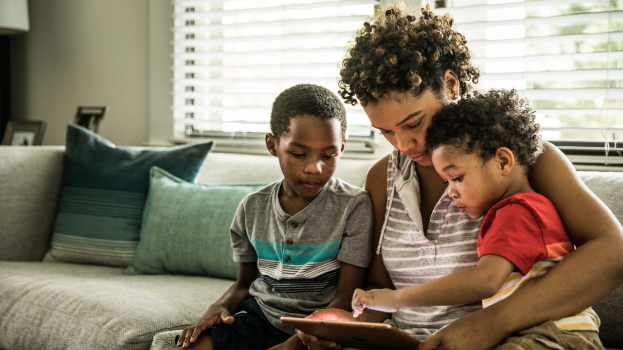 A Black mother using tablet with young sons on couch