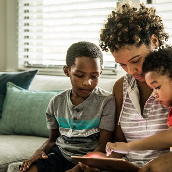 A Black mother using tablet with young sons on couch