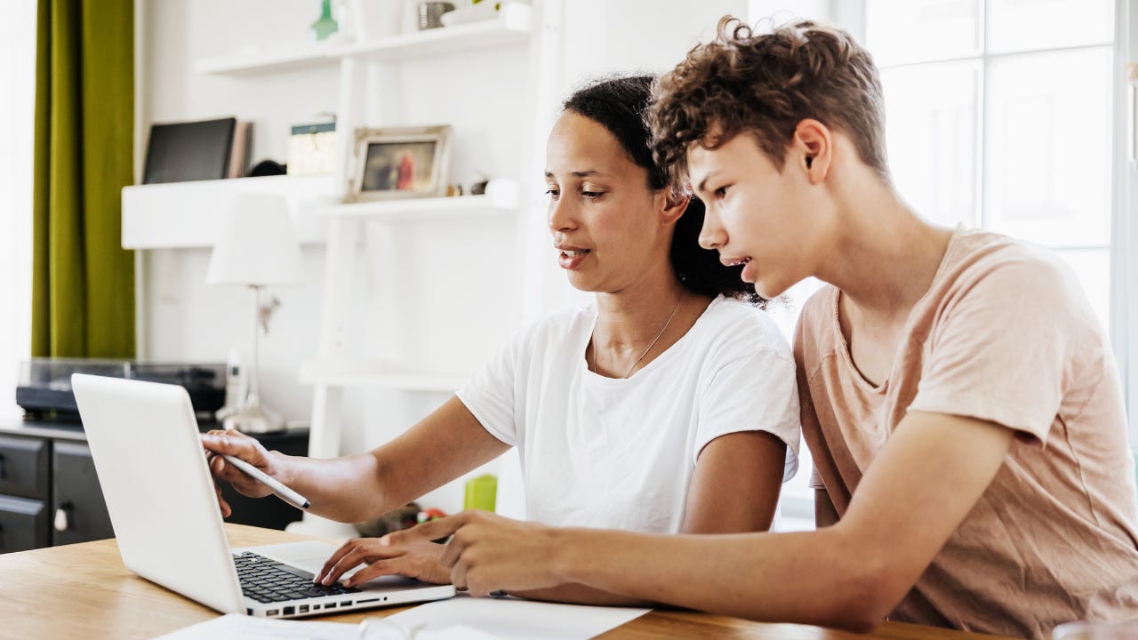 Mother explaining financial topic to young boy sitting at laptop