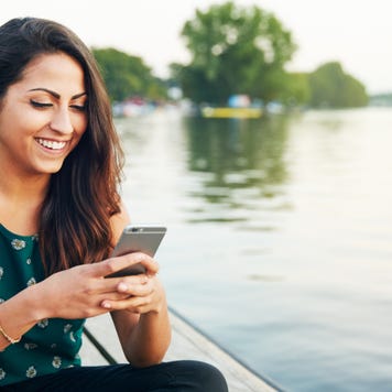 A young woman looks at her phone on a jetty