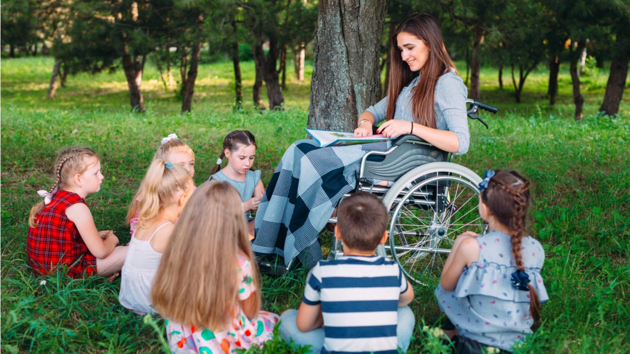 Woman in wheelchair reads aloud to a group of kids