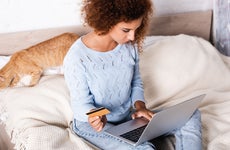 Selective focus of young woman holding credit card and using laptop near tabby cat on bed