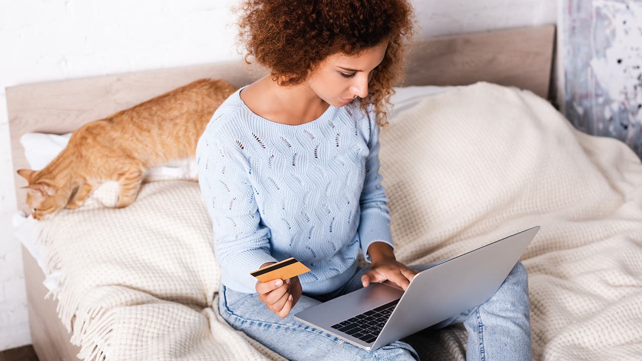 Selective focus of young woman holding credit card and using laptop near tabby cat on bed