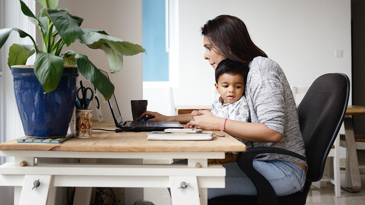 woman holding a child and working online at home