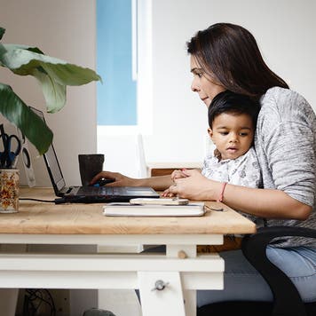 woman holding a child and working online at home