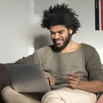 Man sitting on couch in living room with laptop and credit card