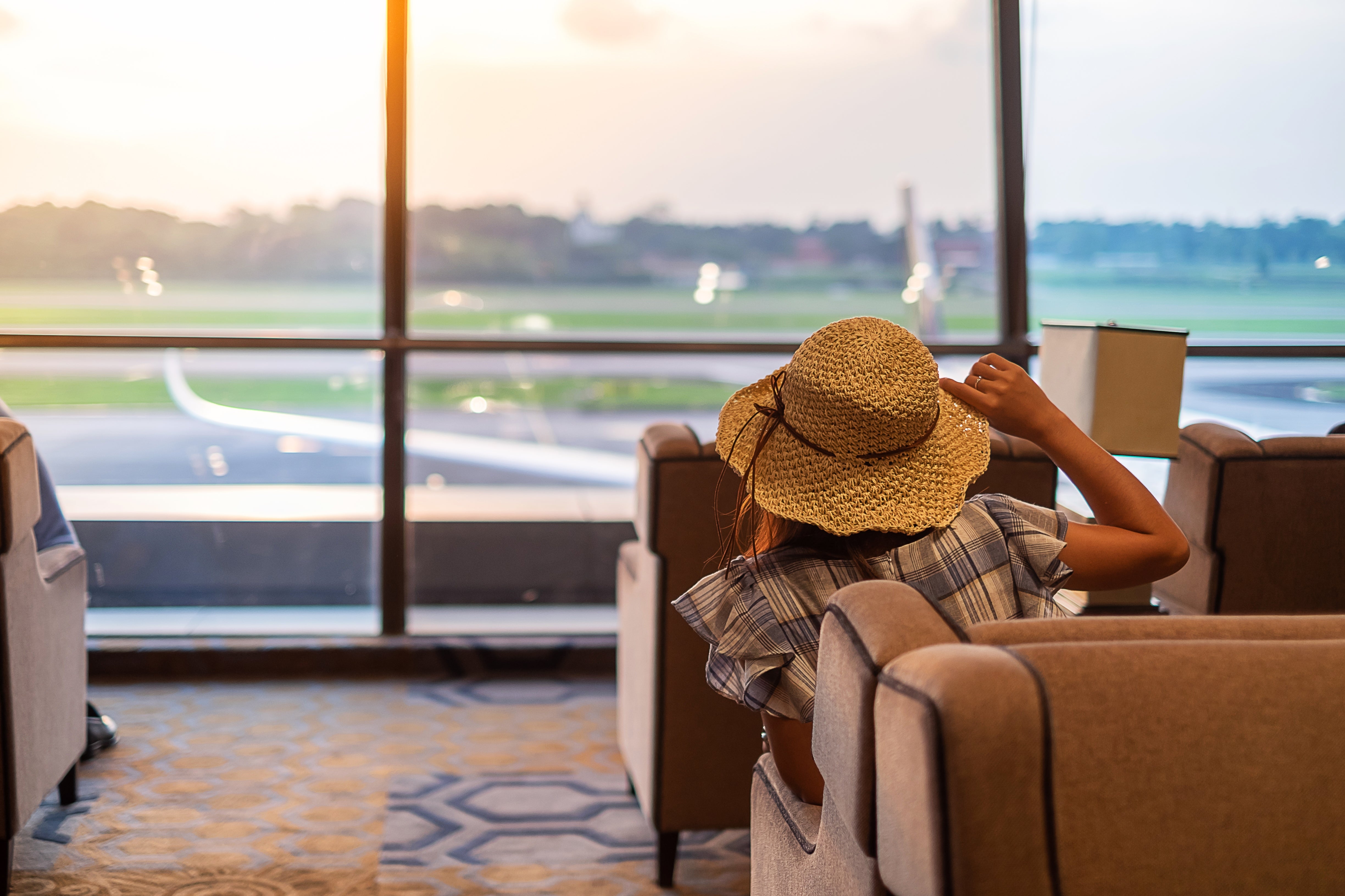 Female traveler with hat looking at airplane from modern airport lounge