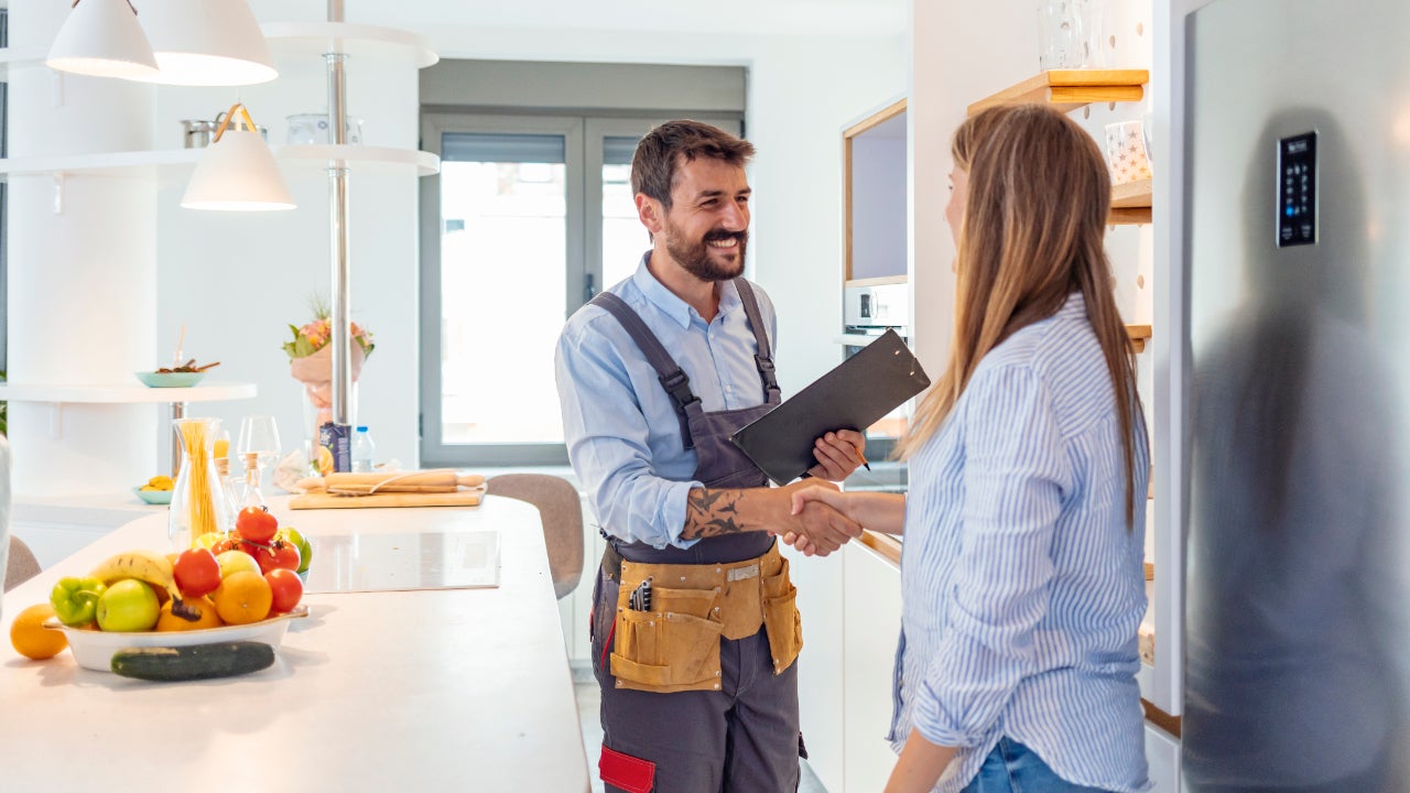 Young Woman Shaking Hands To Male Plumber With Clipboard In Kitchen