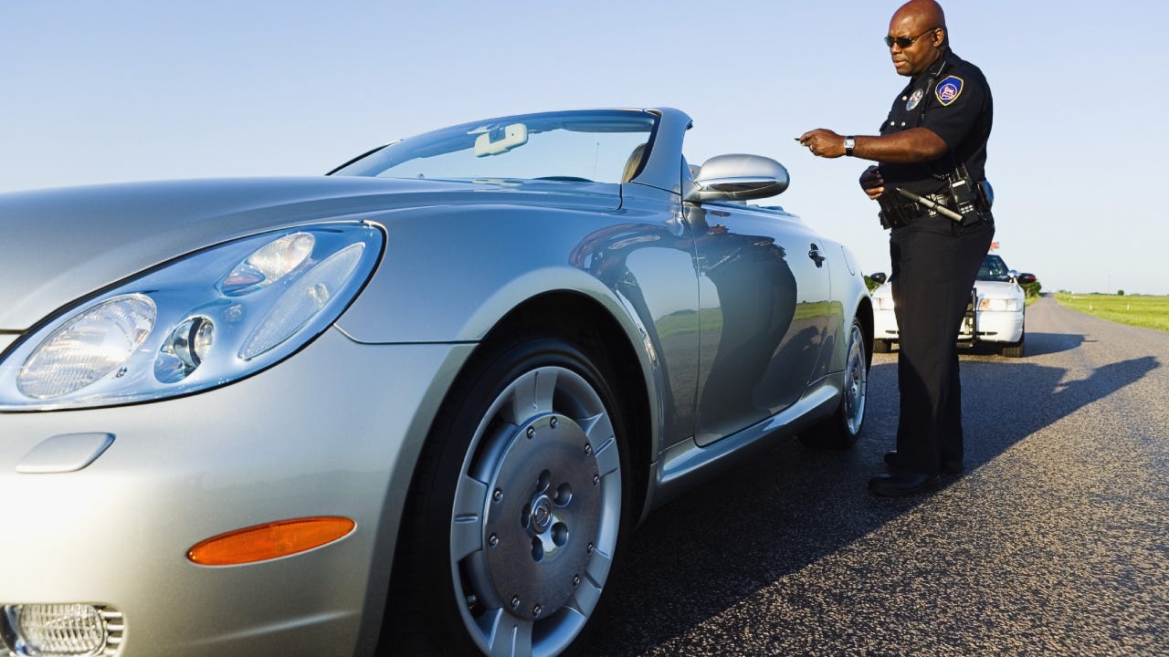 Police officer standing near a convertible car holding a driver's license