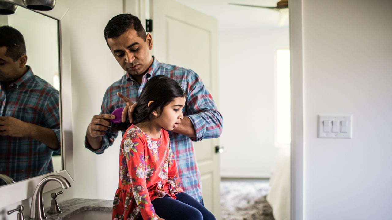 Father brushing daughters hair in bathroom