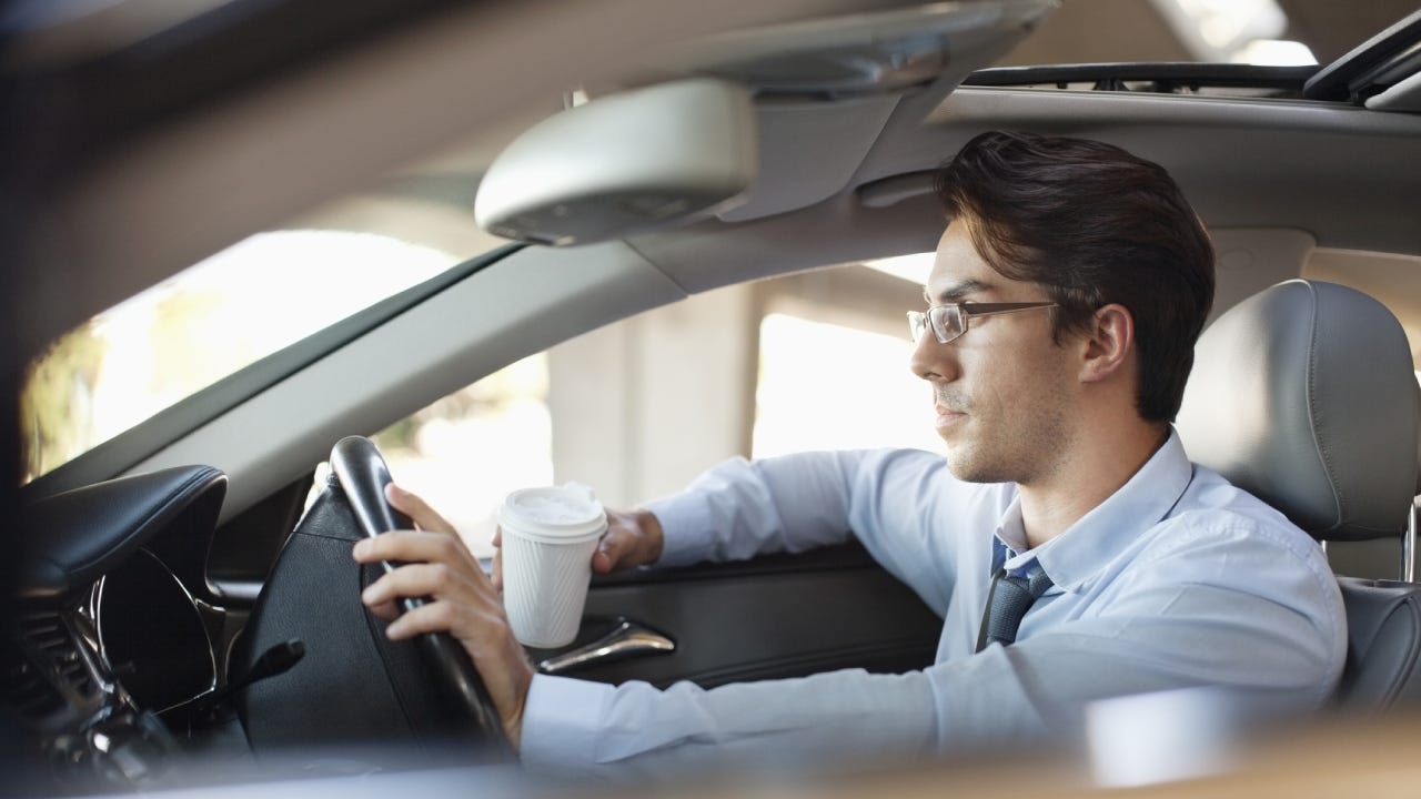 Businessman holding coffee cup and driving car