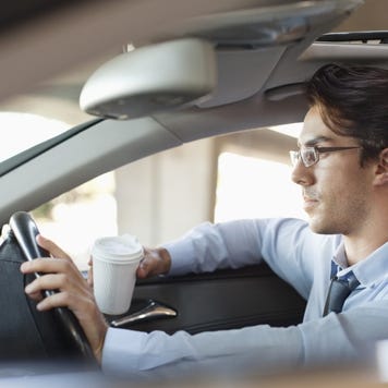 Businessman holding coffee cup and driving car
