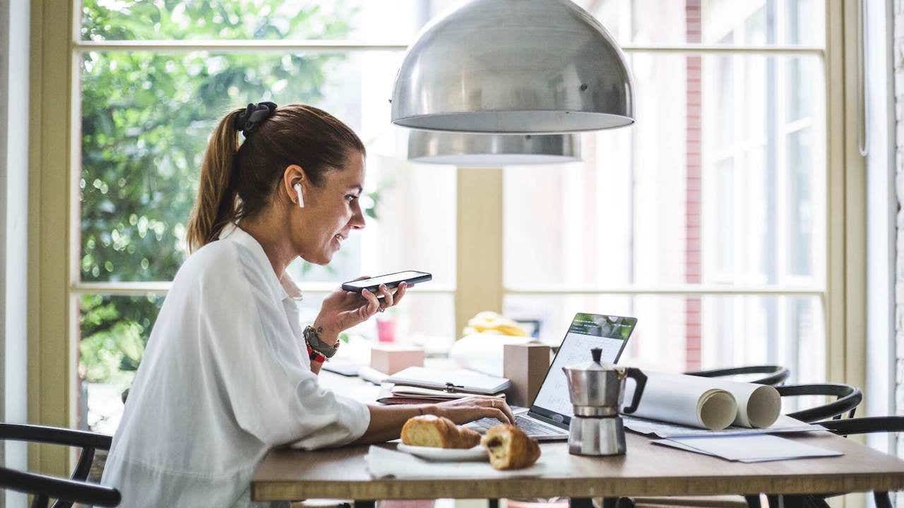 Smiling female entrepreneur using laptop while talking through smart phone at home office