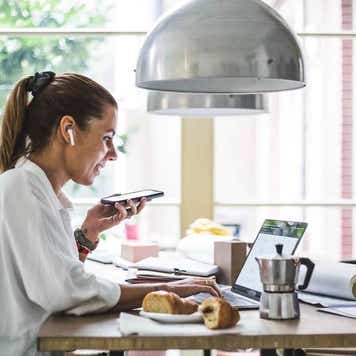 Smiling female entrepreneur using laptop while talking through smart phone at home office