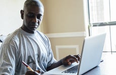 Black man using laptop and notebook at table