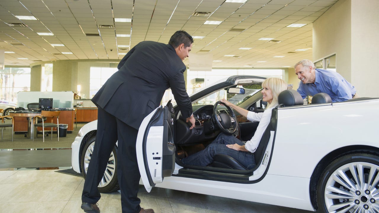 Salesman showing convertible to couple in car dealership