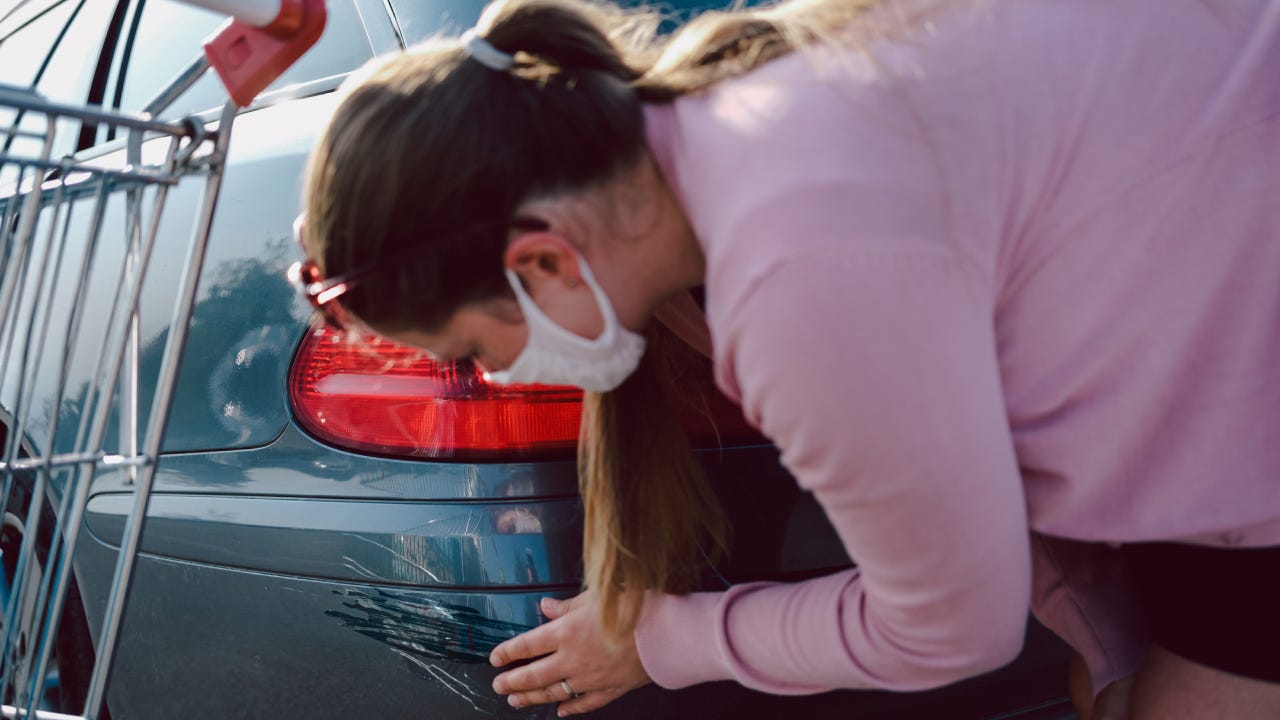 Woman with face mask checking car scratch at supermarket.