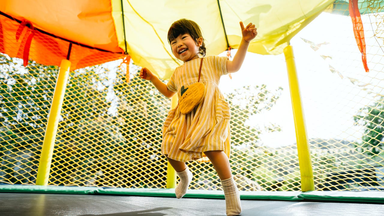 Joyful little Asian toddler girl smiling happily and having fun jumping in a bouncy castle in a outdoor playground