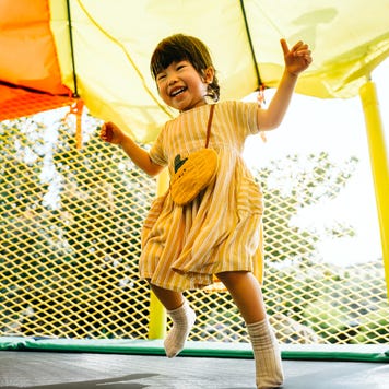 Joyful little Asian toddler girl smiling happily and having fun jumping in a bouncy castle in a outdoor playground