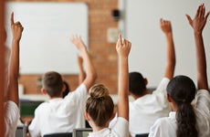 Students in a classroom raise their hands