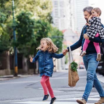 Father with small girls walking outdoors in city, crossing the road