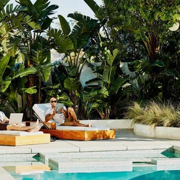 Gay couple working on laptop and digital tablet while relaxing by pool