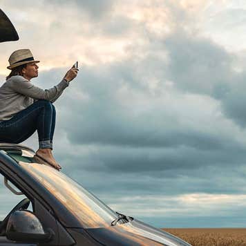 Woman taking a photo whilst sitting on roof of camper at sunset