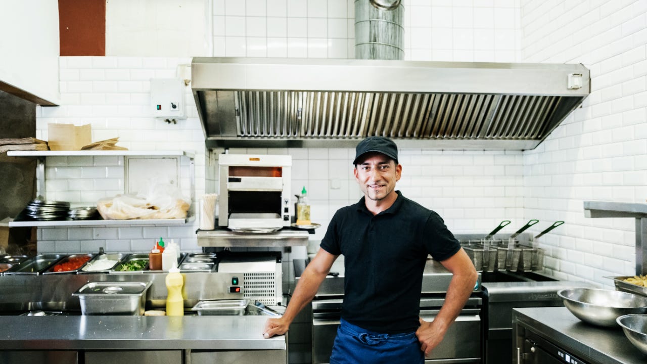 A portrait of a trendy burger restaurant owner standing in his kitchen, smiling