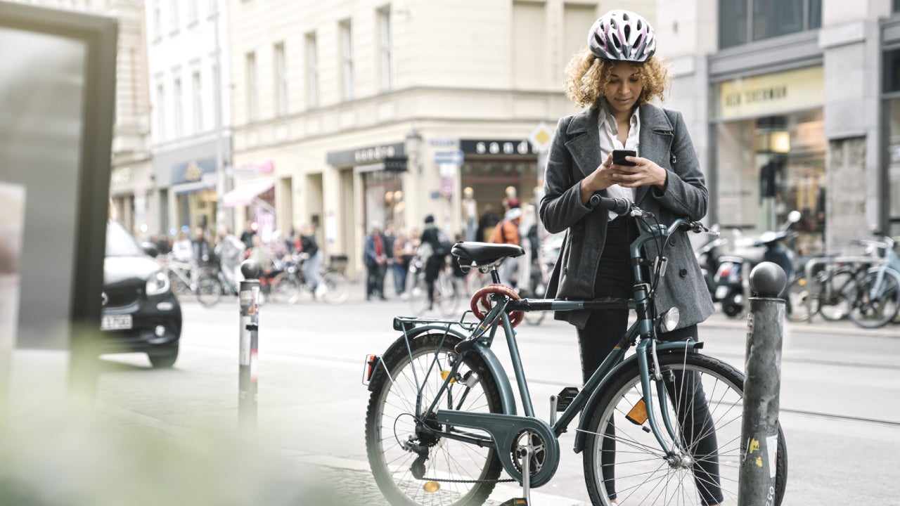Woman with bicycle and smartphone in the city, Berlin, Germany